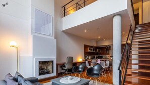 Una sala de estar moderna con un sofá gris, una mesa de centro y una chimenea. Se ve una escalera que sube a un nivel superior.