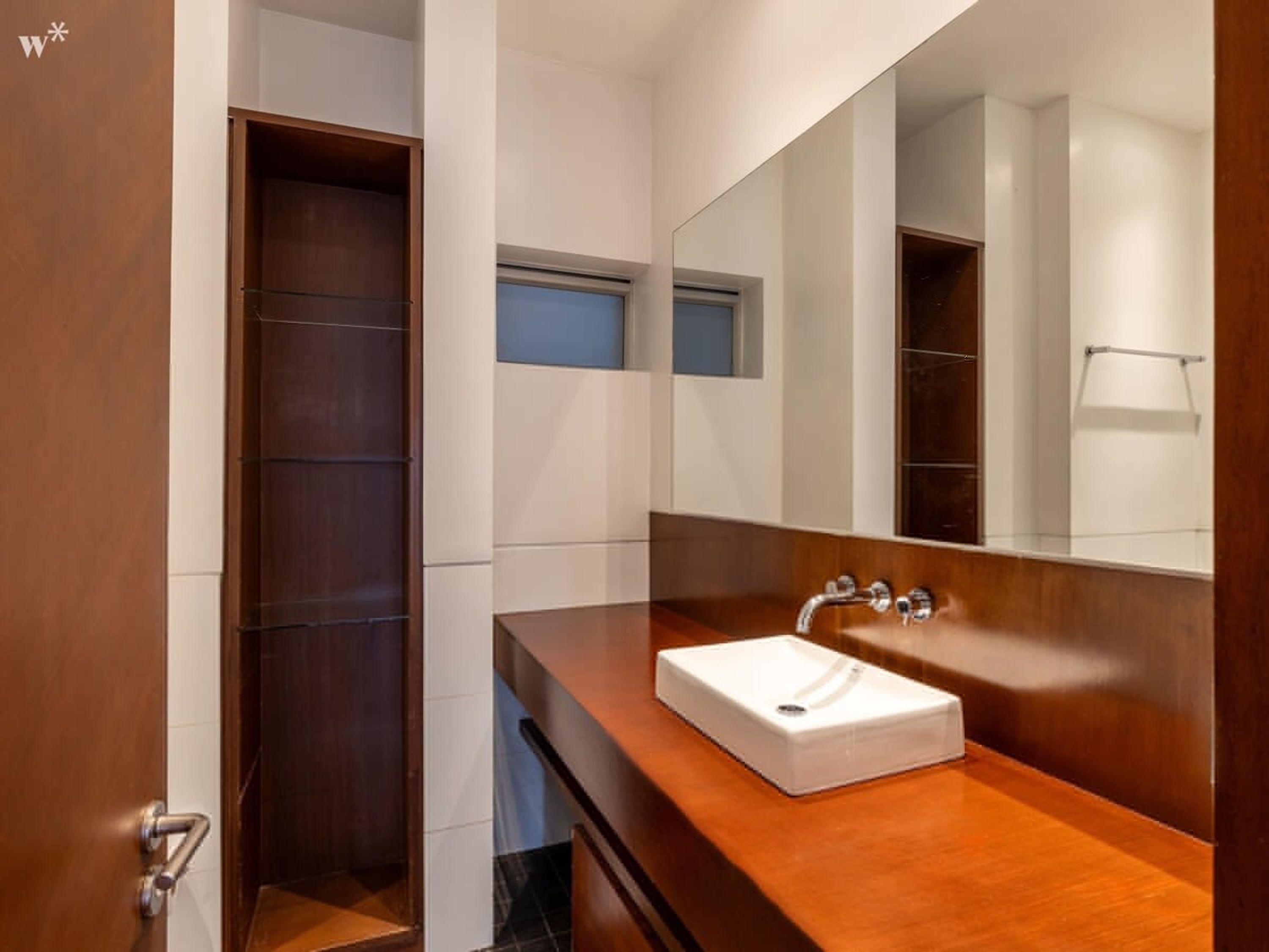 A modern bathroom with a wooden vanity, a white sink, and a large mirror.