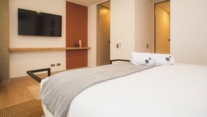 Een moderne hotelkamer met een groot bed, een flatscreen televisie aan de muur, een houten plank en een deur naar een andere kamer.