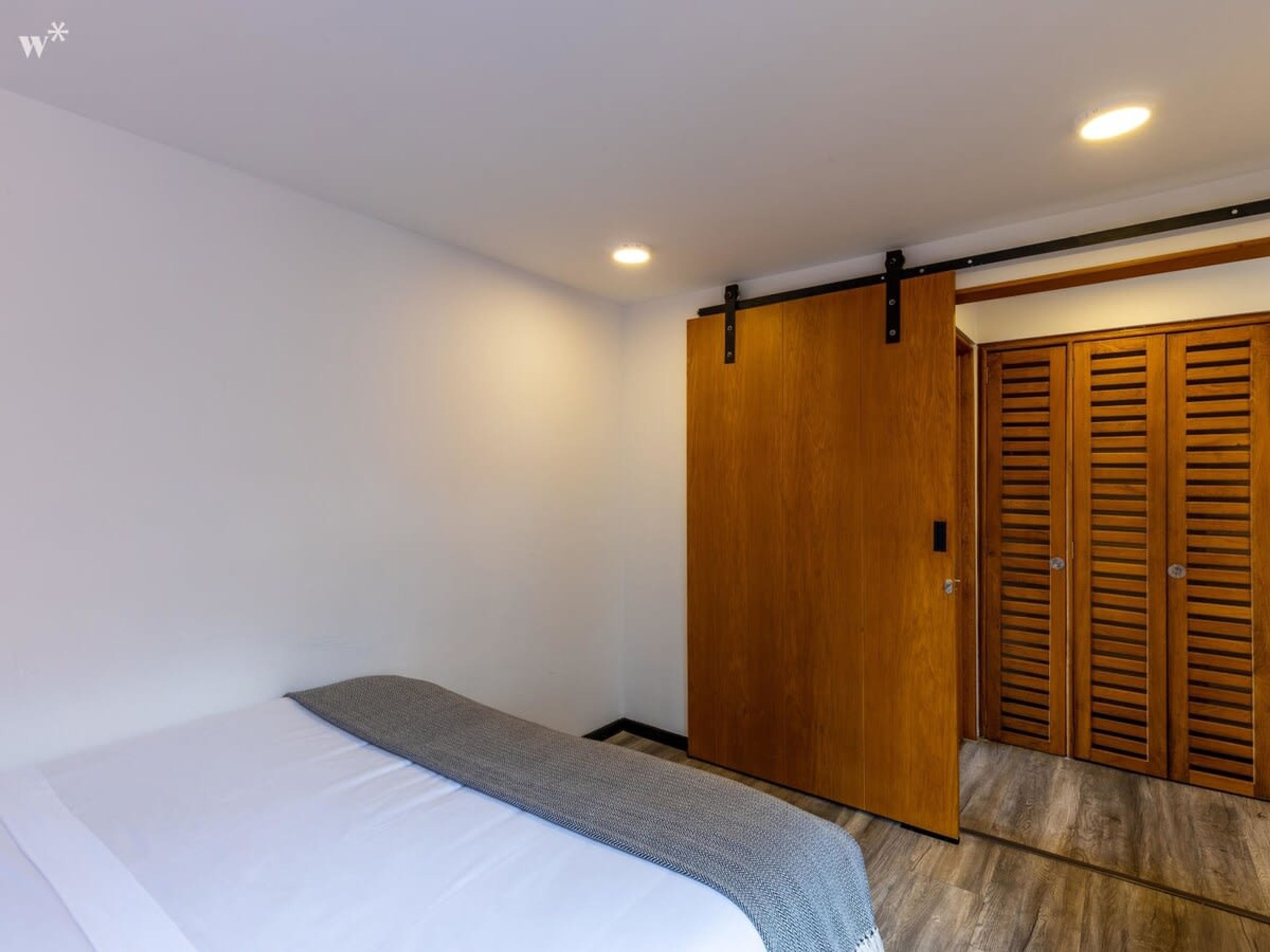 A bedroom with a bed, a wooden wardrobe, and a sliding door closet.