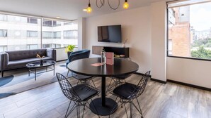 A modern living room with a round table, black chairs, a sofa, and a TV mounted on the wall.