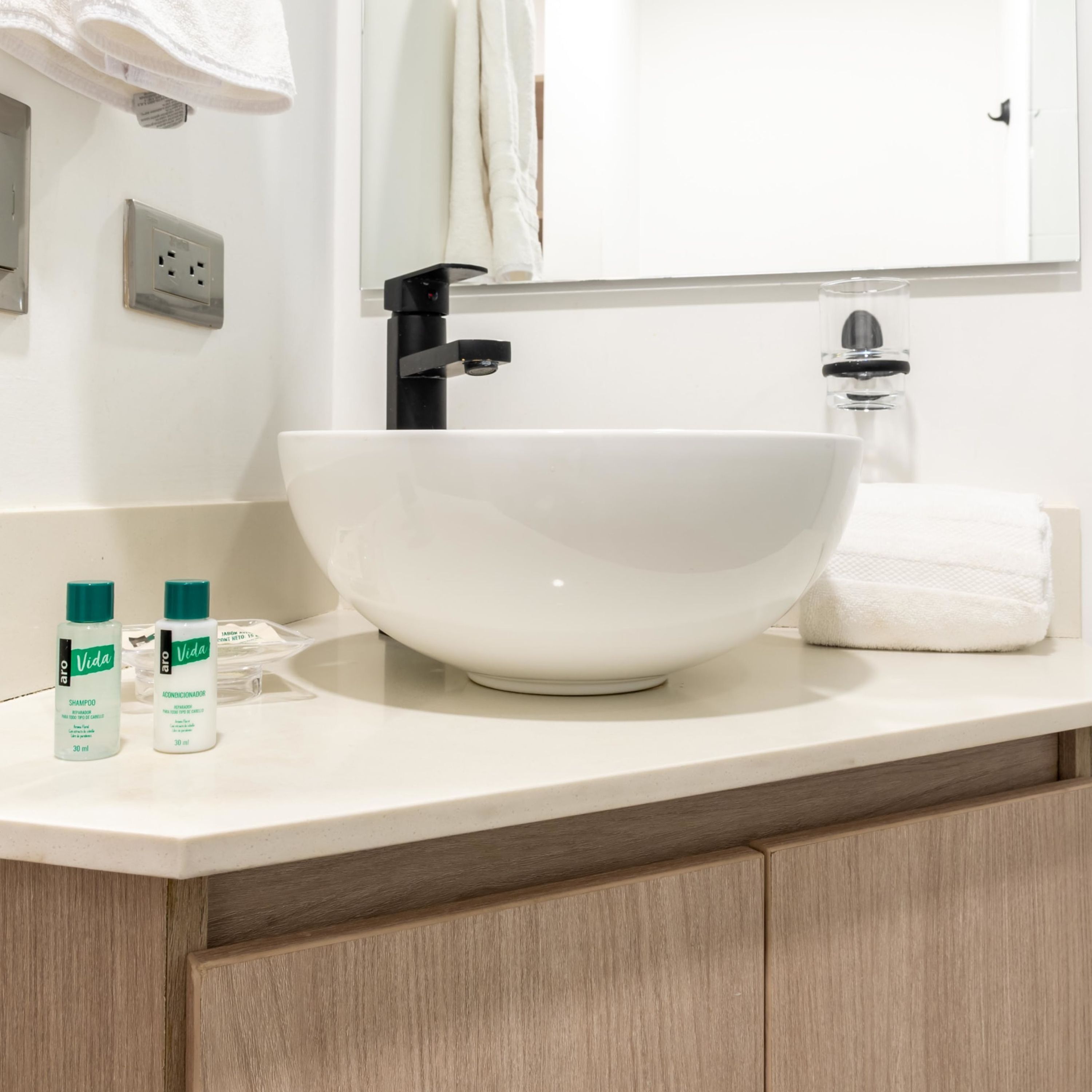 A bathroom with a white sink, a mirror above it, and two bottles of shampoo on the counter.
