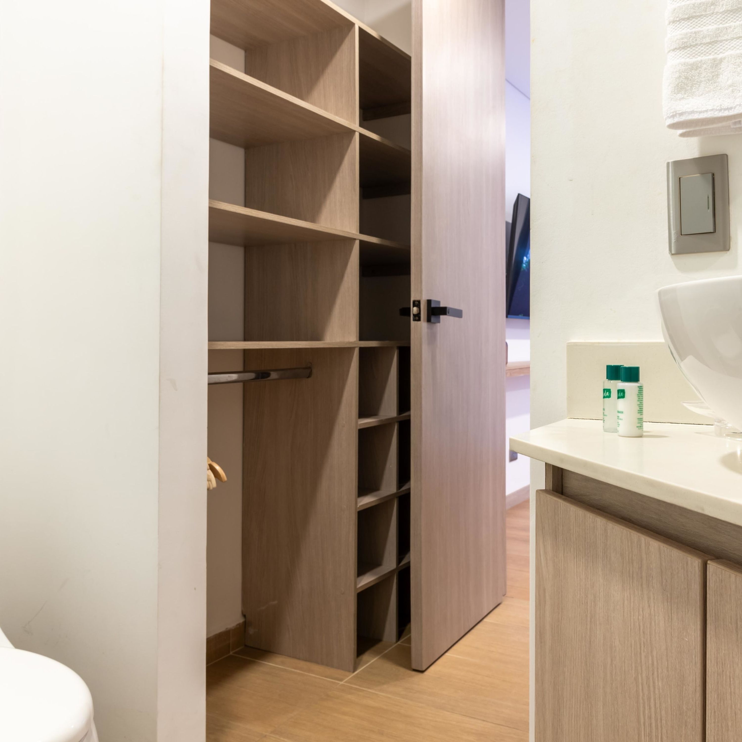 A modern bathroom with a wooden vanity, a toilet, and a walk-in closet with shelves.