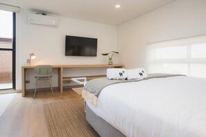 A modern bedroom with a bed, a desk, a chair, a TV, and a window. - Jungle Style 1BR in Laureles (Medellín)