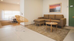 A modern living room with a sectional sofa, a wicker chair, and a small coffee table. - Jungle Style 1BR in Laureles (Medellín)