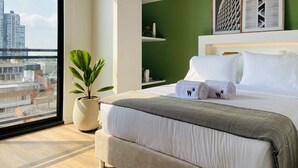 A modern hotel room with a large bed, a potted plant, and a city view. - w Loft in Chapinero (Bogotá)