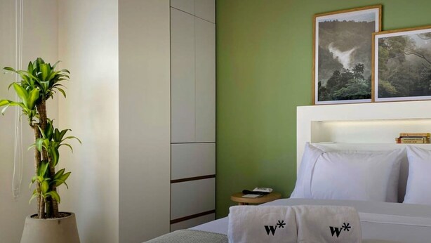 A hotel room with a bed, a nightstand, a potted plant, and two framed pictures on the wall. - w Loft in Chapinero (Bogotá)