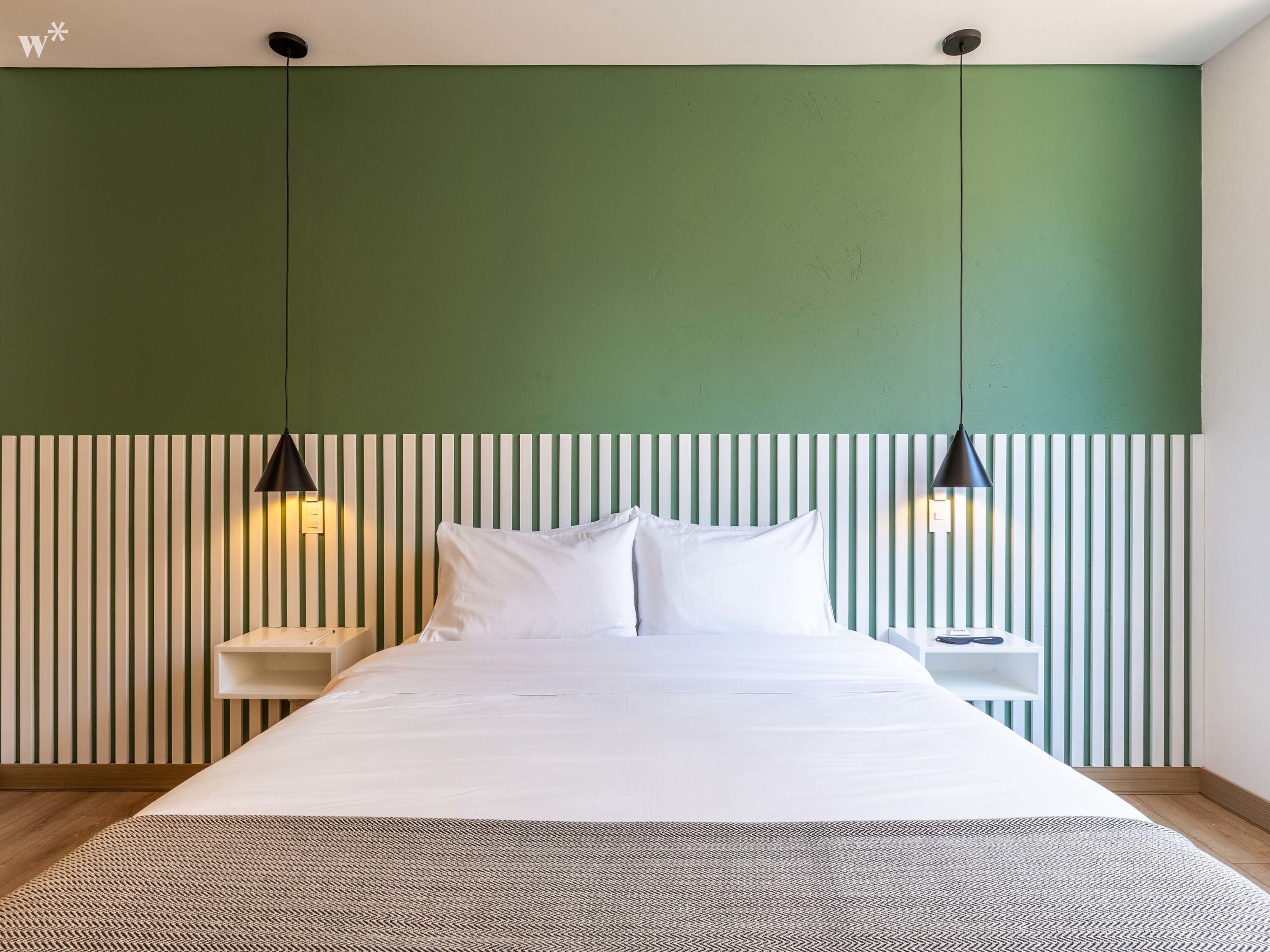 A modern bedroom with a green accent wall, a white headboard, and two bedside lamps.