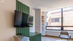 Una habitación moderna con una televisión de pantalla plana montada en un panel verde, una silla blanca, una silla gris y una mesa blanca.