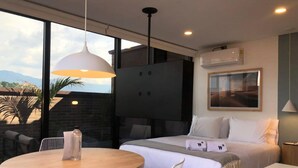 A modern hotel room with a bed, a round wooden table, a TV, and a large window offering a view of palm trees and mountains. - Splendid Loft With Terrace in Laureles (Medellín)