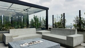 A rooftop terrace with a fire pit, seating areas, and a glass enclosure overlooking a cityscape. - w Artistic Loft in Unique Building (Bogotá)