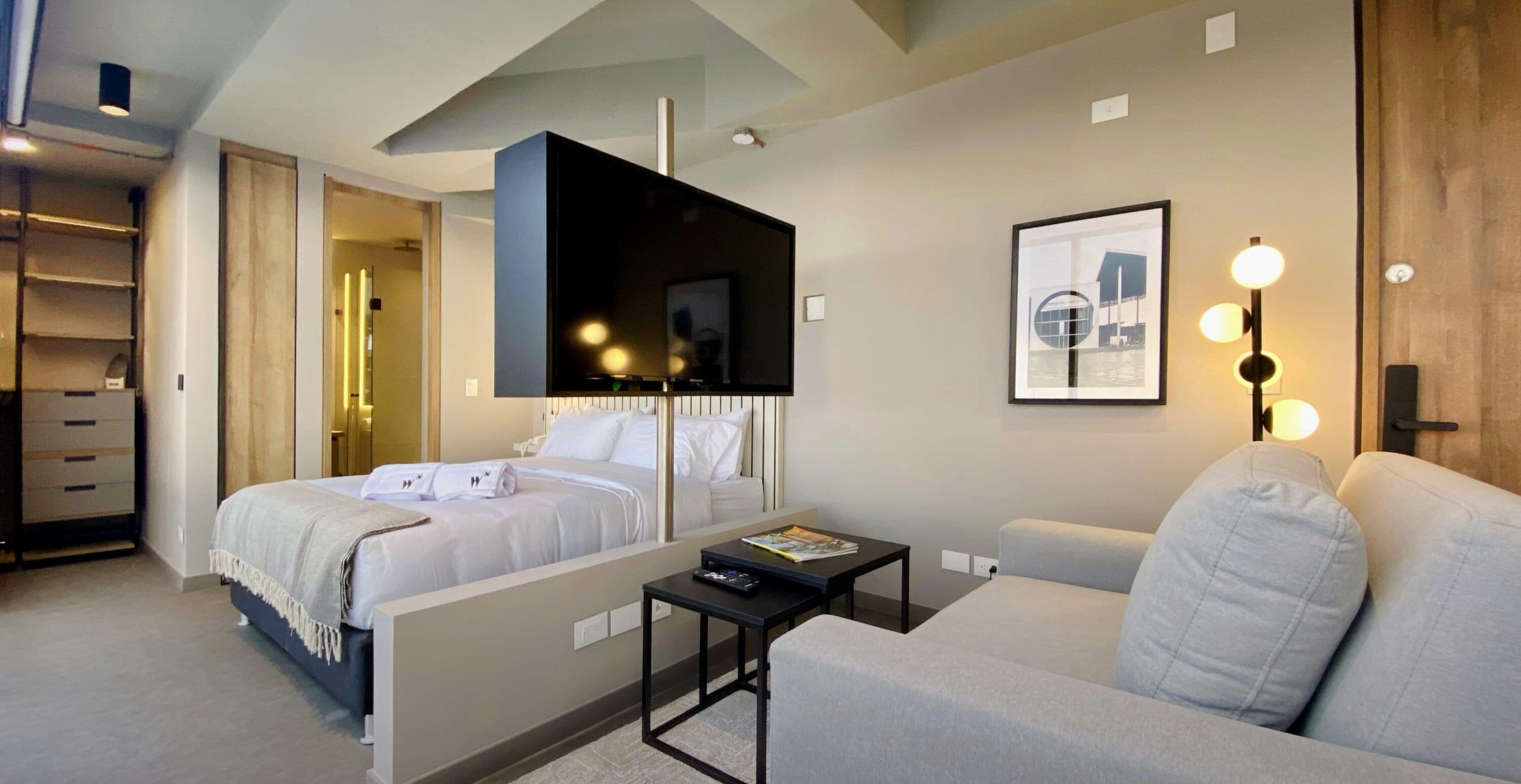 A modern hotel room with a bed, a sofa, a TV, and a framed picture on the wall.