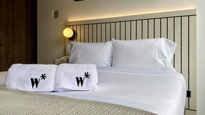 A hotel room with a bed, two white towels with black 'W' symbols, a bedside lamp, and a wooden door. - w Artistic Loft in Unique Building (Bogotá)