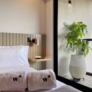 Une chambre d’hôtel moderne avec un lit, une table de chevet, une lampe et une plante en pot.