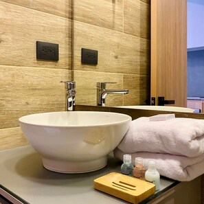 A bathroom with a large white sink, a mirror, and wooden paneling on the wall.