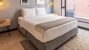 A modern bedroom with a large bed, a nightstand, a wall-mounted lamp, and framed pictures. - Modern 1BR in Cabrera (Bogotá)