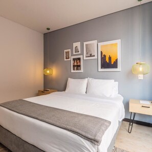 A neatly made bed with white linens, a gray throw blanket, and a cityscape picture on the wall.