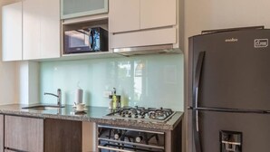 A modern kitchen with a built-in oven, a gas stove, a black refrigerator, and white cabinetry. - Modern 1BR in Cabrera (Bogotá)
