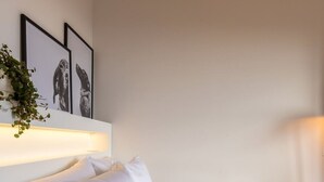 A neatly made bed with white linens and pillows, a wall-mounted shelf with framed pictures, and a potted plant. - w Modern Loft in Chapinero (Bogotá)