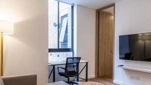 Ein modernes Wohnzimmer mit einer Couch, einem Esstisch mit Stühlen, einem an der Wand befestigten Fernseher und einem großen Fenster mit Blick hinaus.