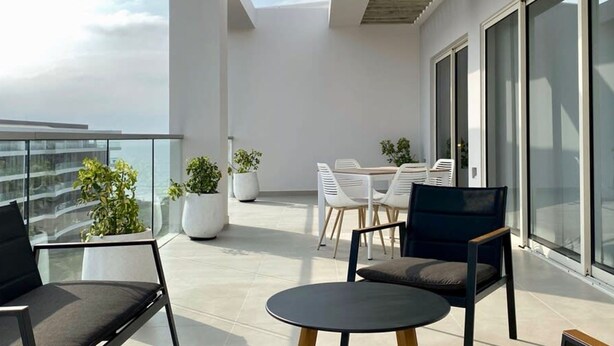 Un balcon extérieur moderne doté d’une rambarde en verre, de plantes en pot et de mobilier contemporain.