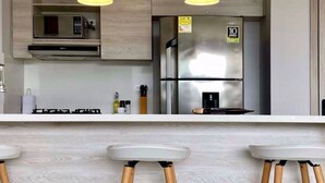 Une cuisine moderne dotée de deux luminaires suspendus, d’un réfrigérateur en acier inoxydable et d’un four encastré.