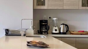 Une cuisine moderne dotée d’un plan de travail blanc, d’une machine à café, d’un mixeur et d’une bouilloire.