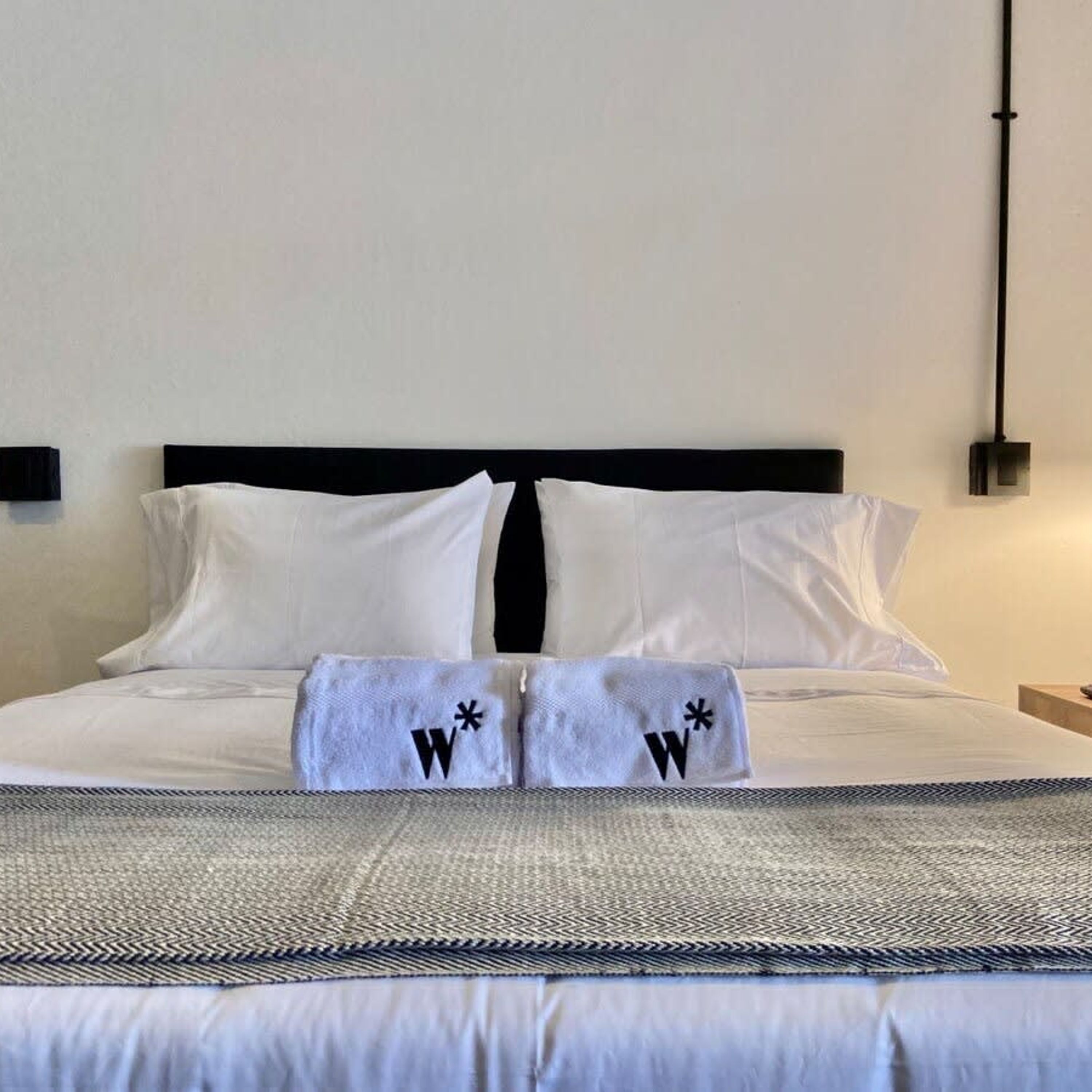 Una cama bien hecha con sábanas blancas y dos toallas con la letra 'W' bordada.