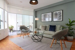 Relax in this stylish living space with a sofa, coffee table, and chairs, surrounded by a large window and lush greenery.