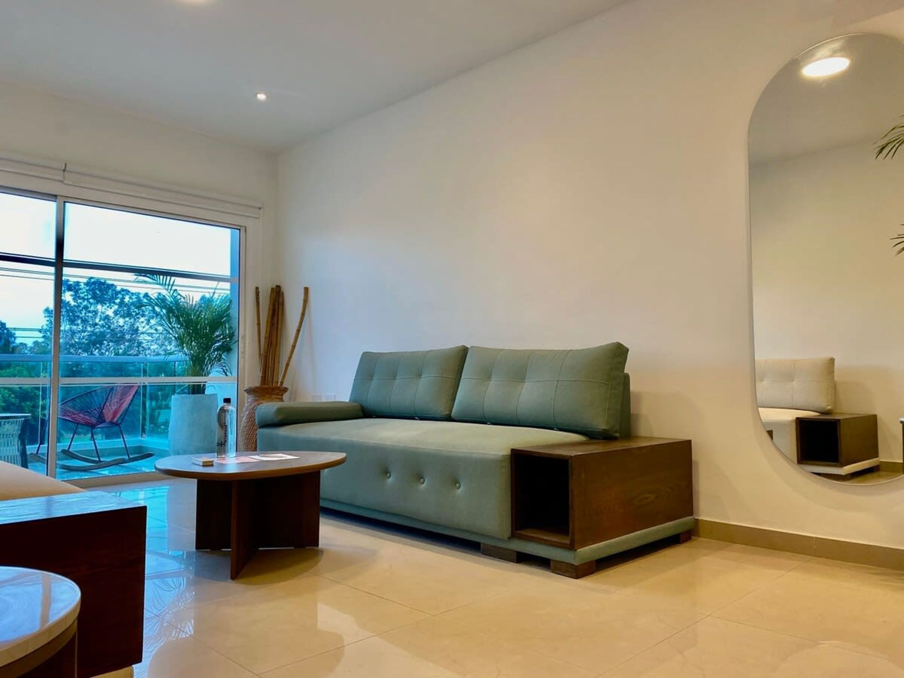 A modern living room with a sofa, a coffee table, and a chair. There is a large window providing a view of the outdoors.