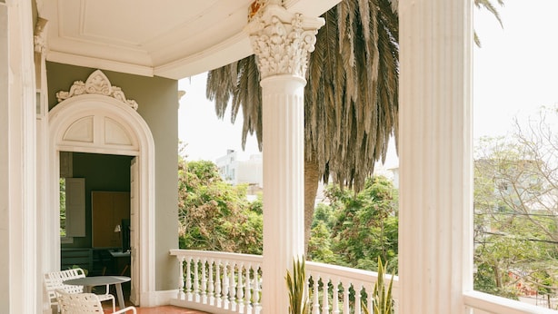A covered porch with white columns, a white railing, and potted plants. - w Astonishing Casa Centenario in Barranco (Lima)
