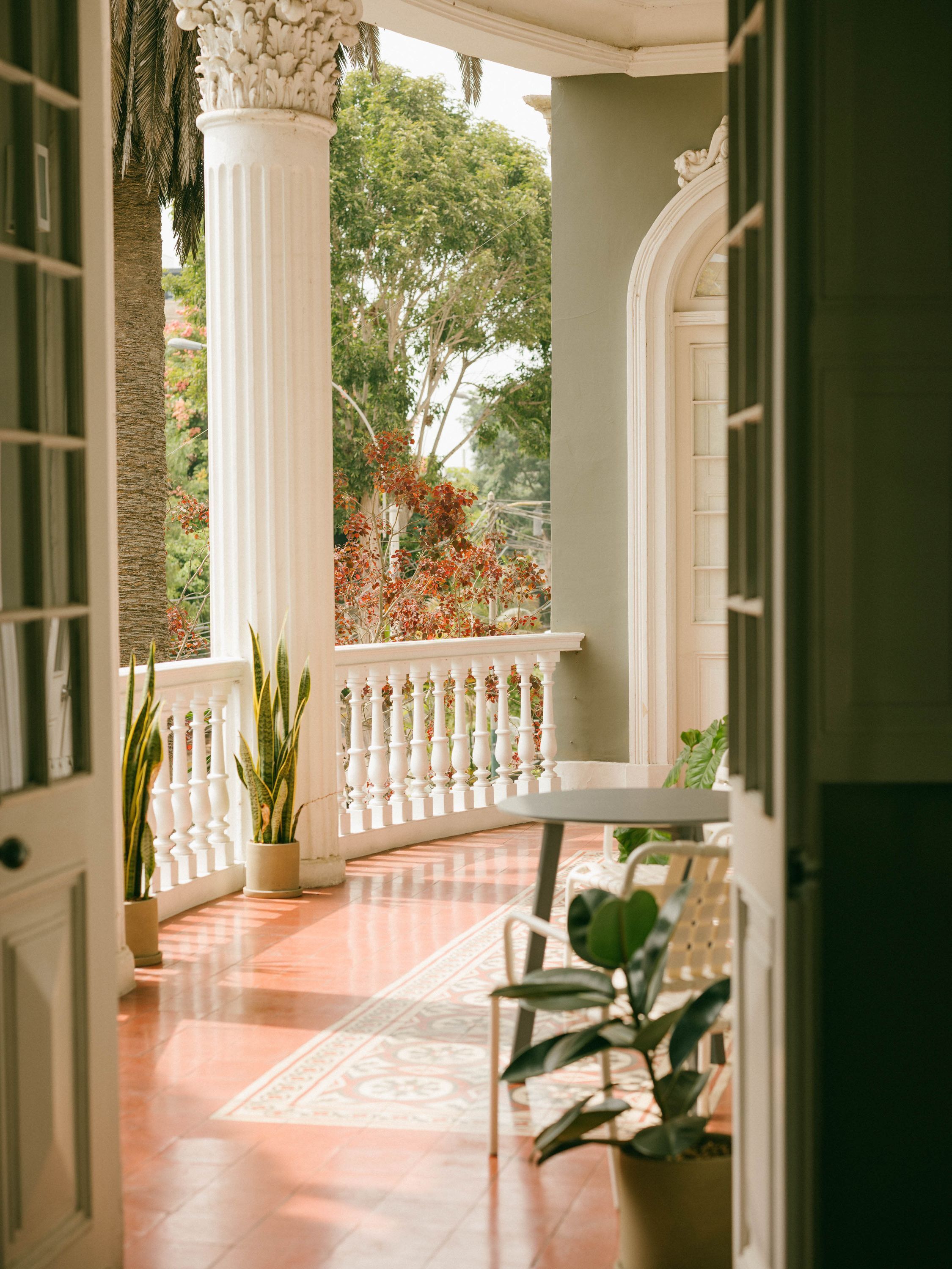 Une véranda couverte avec une balustrade blanche, des plantes en pot et un sol carrelé.