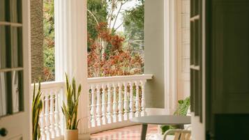 Une véranda couverte avec une balustrade blanche, des plantes en pot et un sol carrelé.