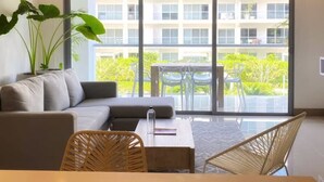 A modern living room with a sofa, a dining table, and chairs. There is a large window with a view of a building and greenery outside. - w Fantastic 2BR w AC in Sunny Cartagena (Cartagena)