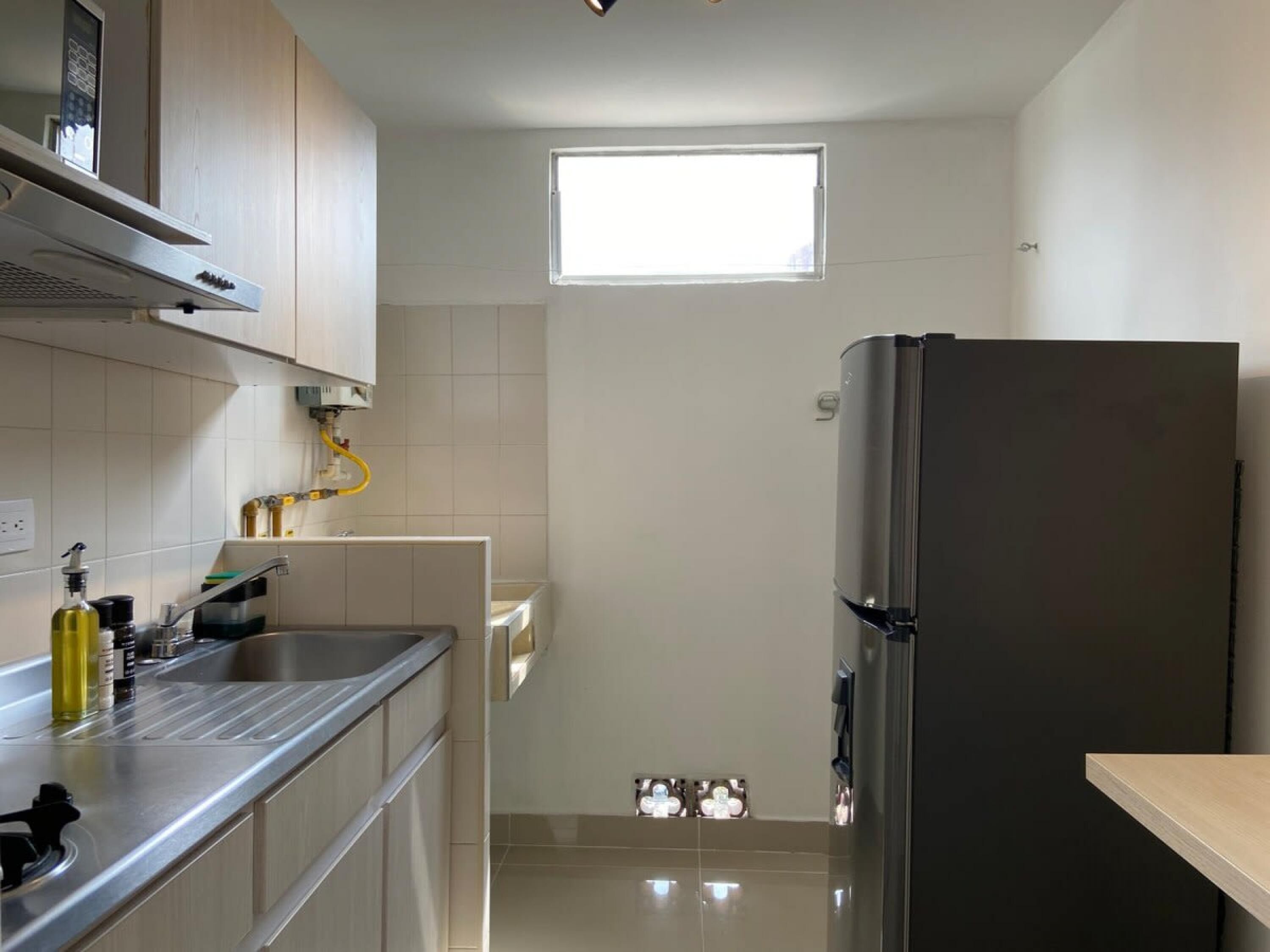 Una cocina compacta con un refrigerador de acero inoxidable, una ventana y un lavamanos con varios objetos sobre la encimera.