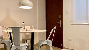 Un comedor con una mesa y sillas blancas, una lámpara colgante y una puerta de madera.