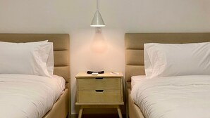 Una habitación de hotel con dos camas, una mesita de noche con cajones y una lámpara colgante.