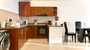 A modern kitchen with wooden cabinets, a built-in oven, a microwave, and a coffee maker. There is a washing machine and a dining area with a table and chairs. - w Oceanview 2BR w/ Terrace n AC in El Laguito (Cartagena)