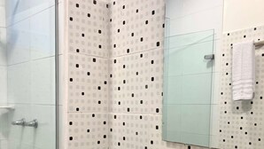 A bathroom with a glass shower enclosure, a toilet, a sink with a mirror above it, and tiled walls with a pattern of squares and dots. - w Oceanview 2BR w/ Terrace n AC in El Laguito (Cartagena)