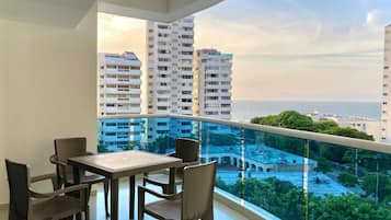 A balcony with a table and chairs, overlooking a cityscape and the sea.