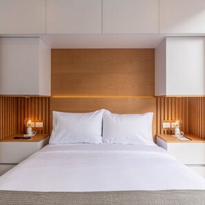Ein modernes Hotelzimmer mit einem hölzernen Kopfteil, weißer Bettwäsche und Nachttischlampen.