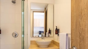 Un baño moderno con cabina de ducha de vidrio, un lavabo blanco con tocador de madera y un espejo sobre el lavabo.