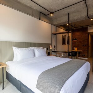 Une chambre d’hôtel moderne avec un grand lit, un petit bureau, un coin repas et un mur en briques.