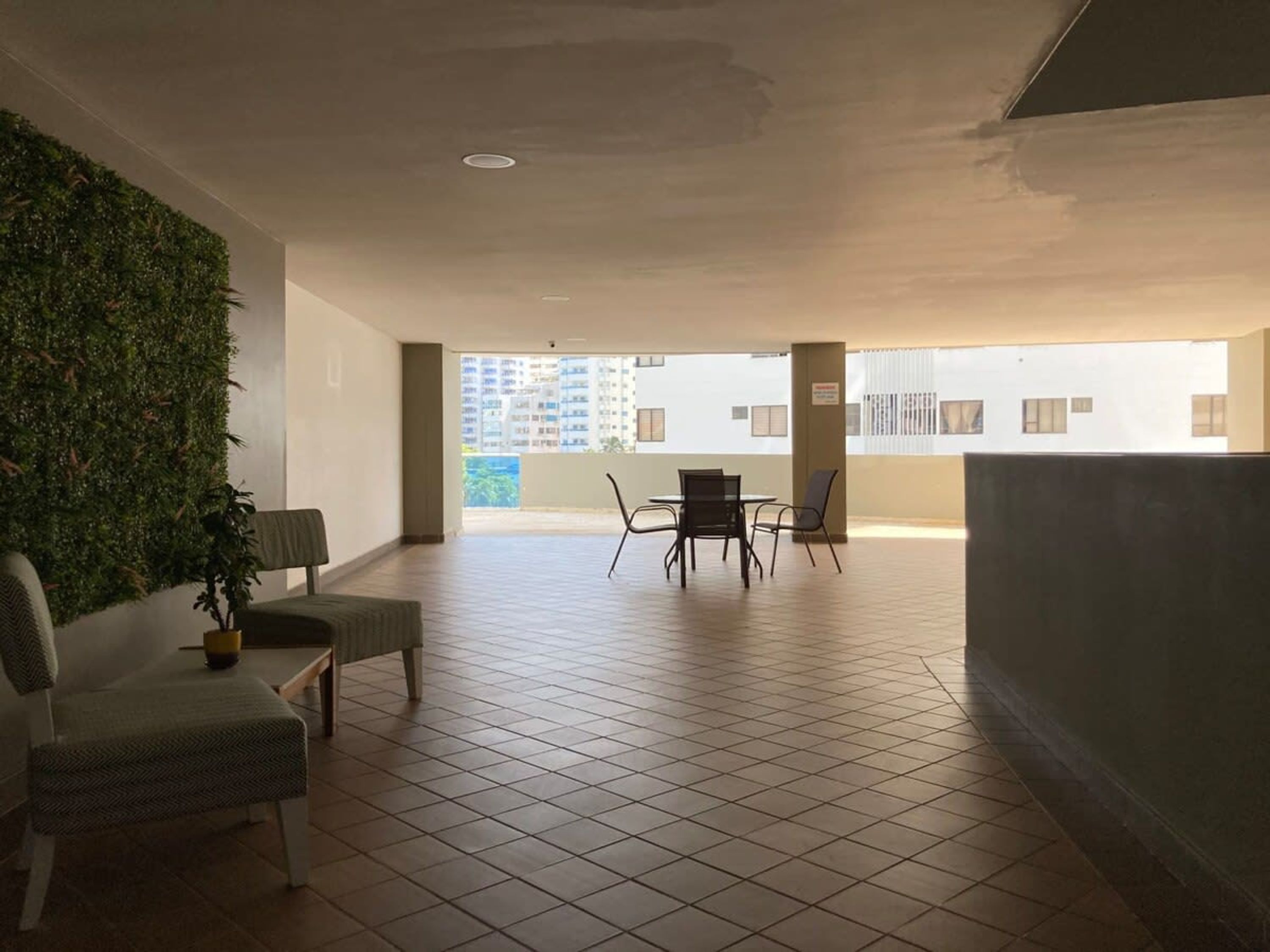 Un balcon spacieux doté d’un sol carrelé, d’un coin salon avec des chaises et une table, et d’un jardin vertical verdoyant sur un des murs.
