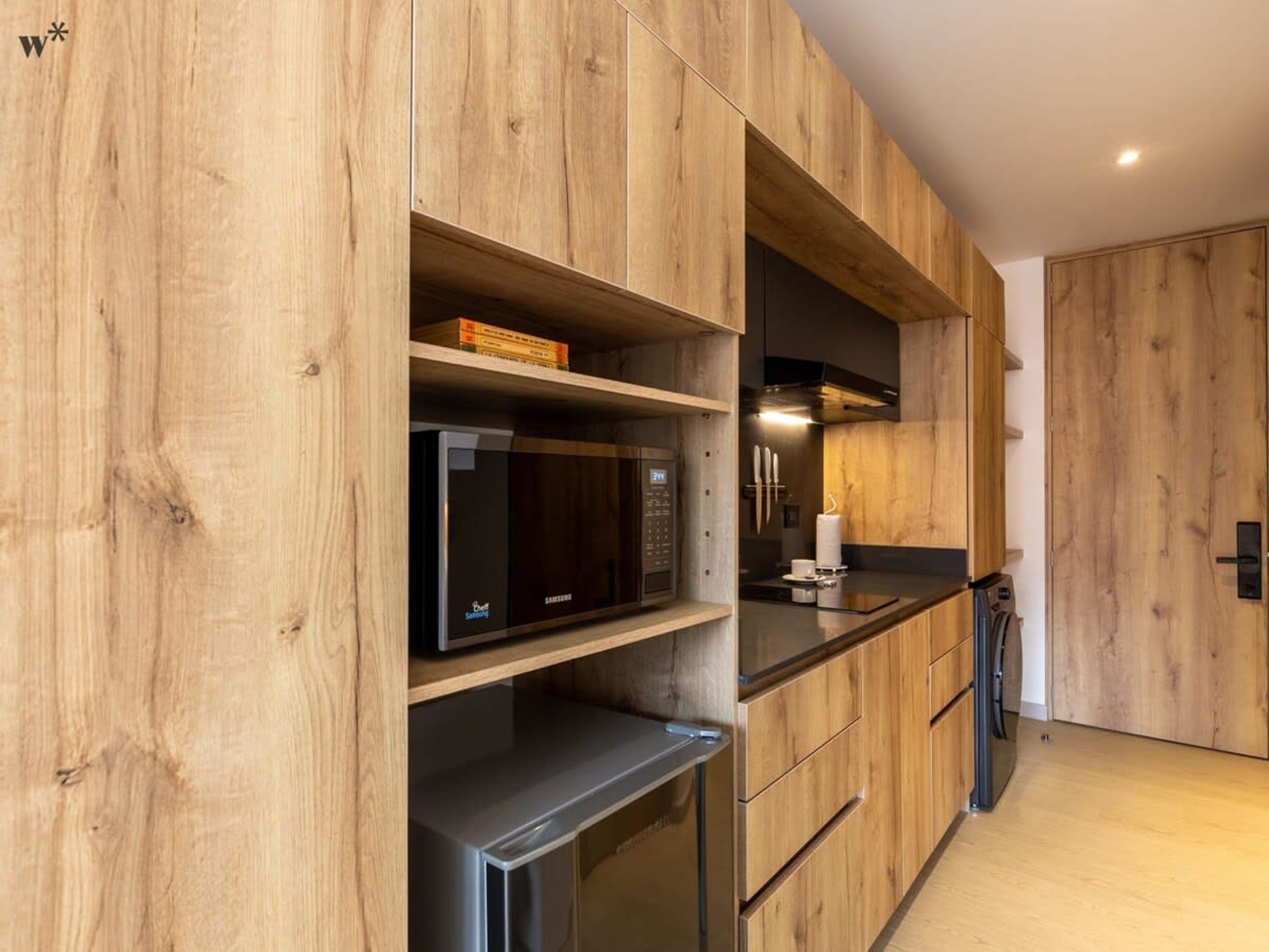 Una cocina moderna con armarios de madera, microondas integrado y refrigerador de acero inoxidable.