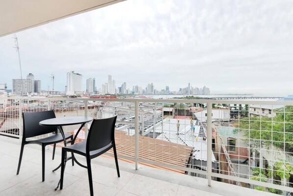 A balcony with a table and chairs, overlooking a cityscape with high-rise buildings and a river. - w Refined 1BR in Casco Antiguo (Panama City)