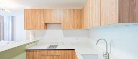 A modern kitchen with wooden cabinets, a white countertop, and a stainless steel faucet.