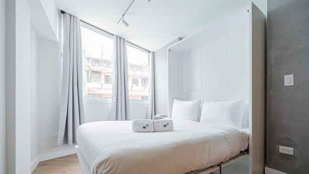 A modern bedroom with a bed, a window with curtains, and a view of buildings outside. - Amazing Loft in Casco Viejo (Panama City)