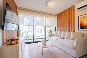 A modern living room with a large window, a sofa, a coffee table, and a TV on a wooden cabinet.