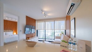 Une chambre d’hôtel moderne équipée d’un lit, d’une télévision, d’une grande fenêtre donnant sur la ville, d’un coin repas et d’un comptoir de réception avec des cartes de bienvenue.
